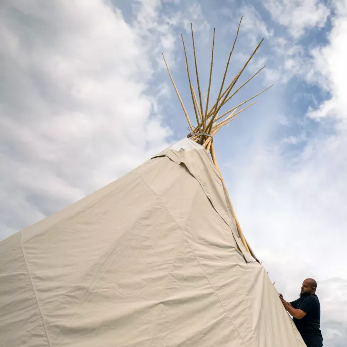 Tipi against cloudy sky with bearded man closing adjusting the canvas